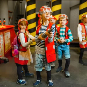 A girl child holding a fire fighting nozzle with some other childs posing as firefighter in a building